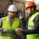 Two manufacturing colleagues in safety equipment discussing a workplace problem